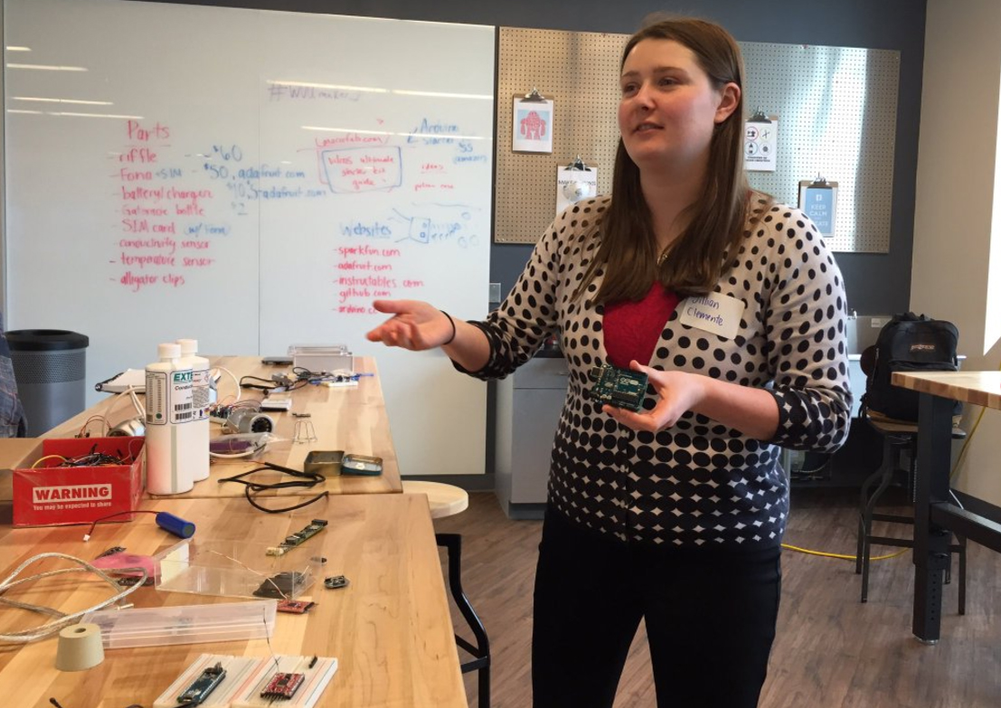 Jillian Clemente As a sophomore Jillian Clemente is pictured in her sensor journalism class with tools she used to build water sensors and other DIY electronics. She is talking to someone (not pictured), and is standing behind a desk covered with other DIY tools. Behind her and the desk is a whiteboard, whose writing is less visible, but is describing various parts and their costs (eg: riffle $60) and websites (eg: instructables.com)